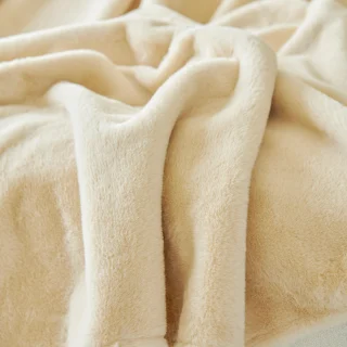 Manta polar gruesa de color beige colocada sobre un sofá, preparada para el invierno.