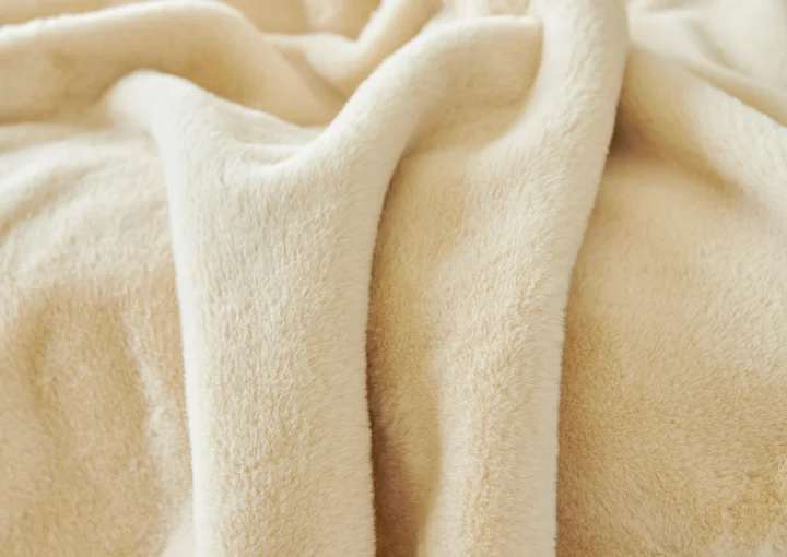 Manta polar gruesa de color beige colocada sobre un sofá, preparada para el invierno.